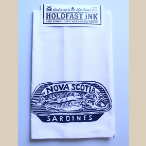 photo of a folded white tea towel with a black screen printed image of an open tin of sardines with the text Nova Scotia Sardines